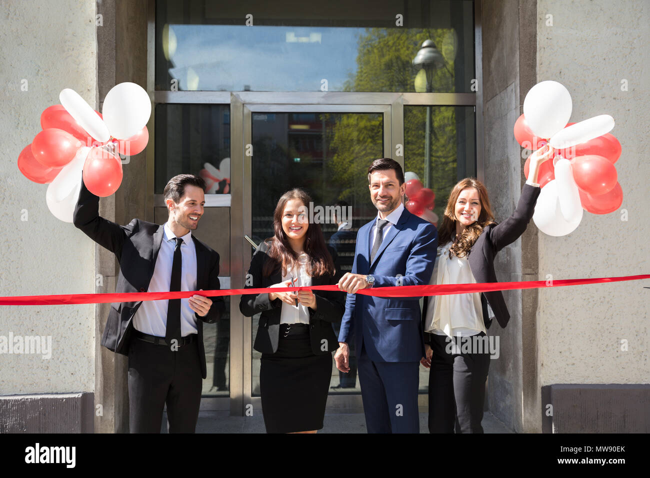 Portrait Of Smiling Young Businesspeople Cutting Red Ribbon Stock Photo