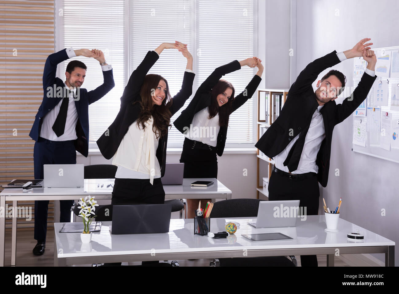 Happy Businesspeople Doing Stretching Exercise Behind Desk At Workplace