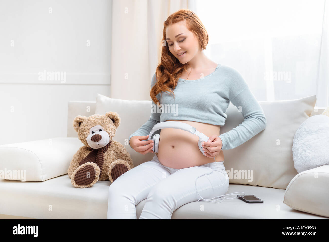 Woman with headphones on pregnant belly Stock Photo by ©Voyagerix 183453360