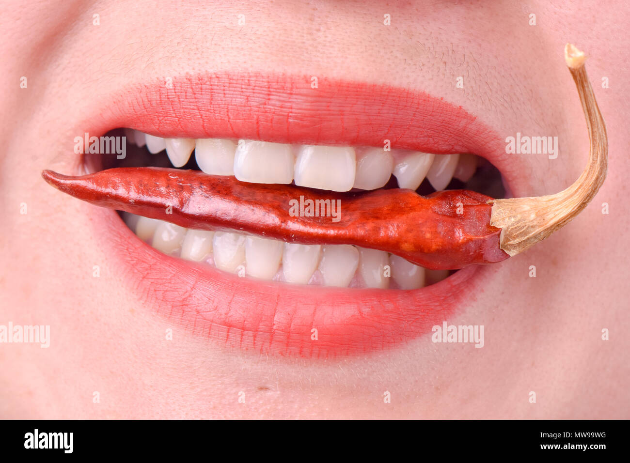 Woman eating a spicy red hot pepper on a white background Stock Photo