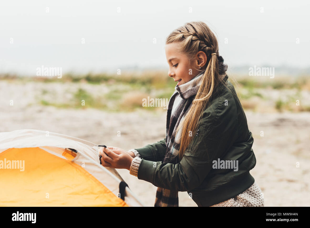 happy little girl installing camping tent on seashore Stock Photo