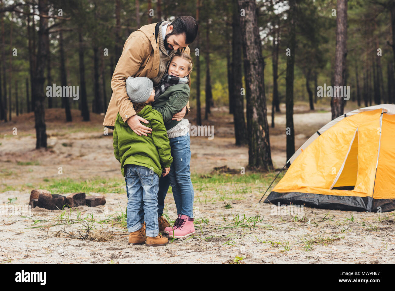 father ambracing with his kids in forest while having camping trip ...