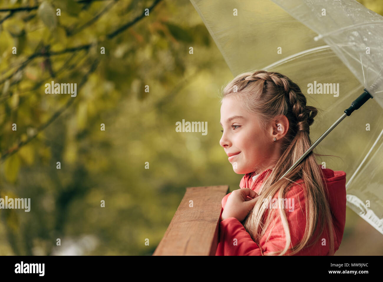 side view of smiling little child holding umbrella and looking away in autumn park Stock Photo