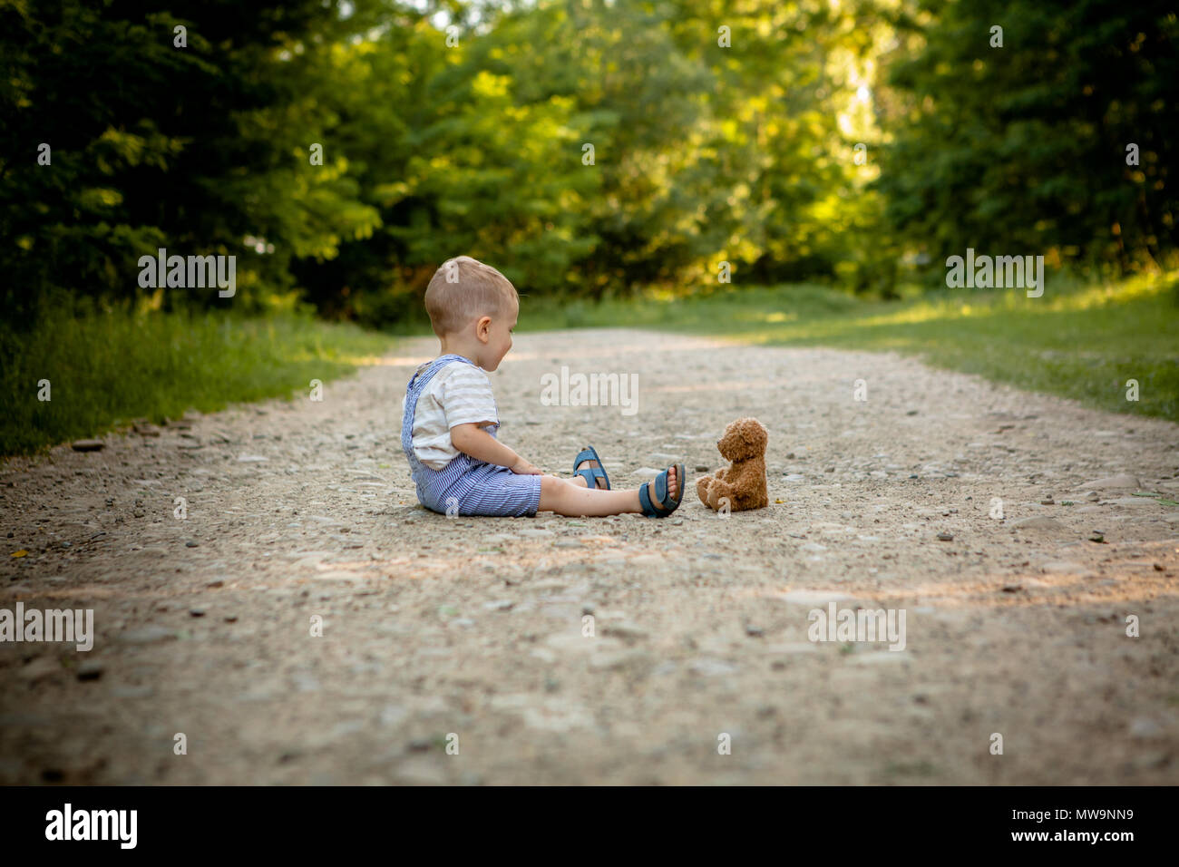 Little boy playing with teddy bear on the footpath Stock Photo - Alamy