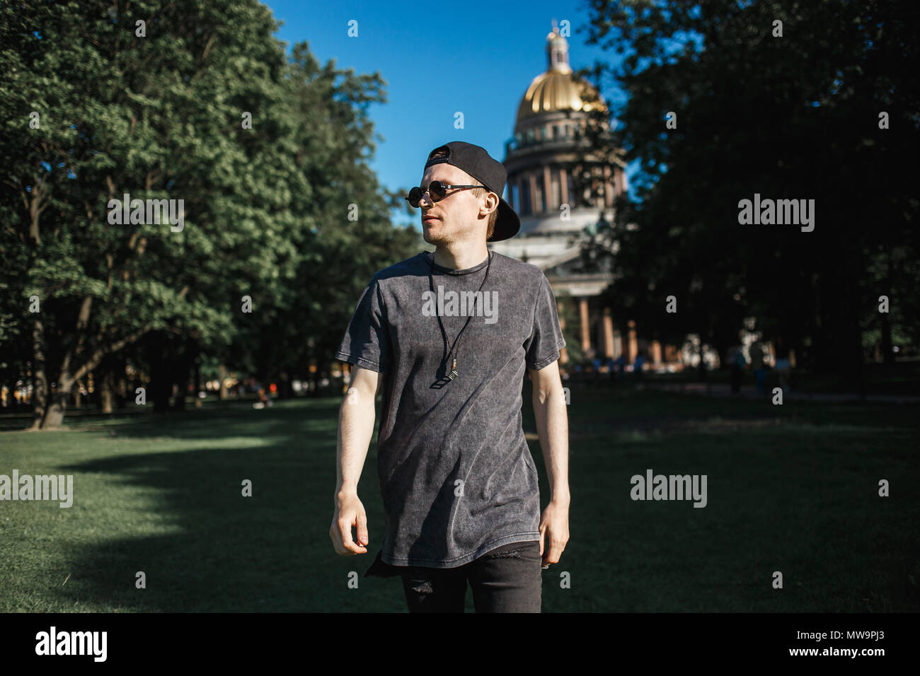 Young stylish man tourist walking on grass near Saint Isaac's Cathedral in Saint-Petersburg in sunny summer day. Stock Photo