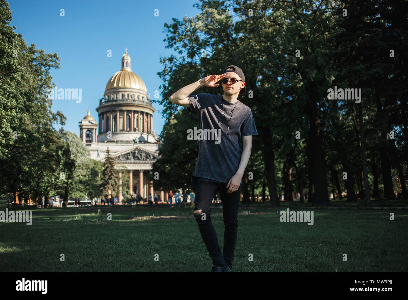 Young stylish man tourist walking on grass near Saint Isaac's Cathedral in Saint-Petersburg in sunny summer day. Stock Photo