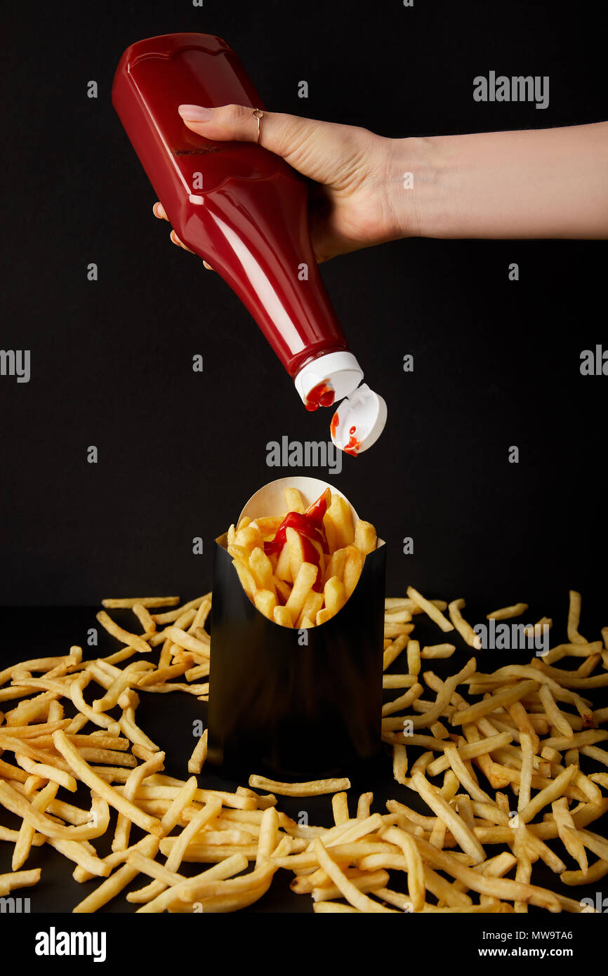 cropped shot of woman pouring ketchup on french fries isolated on black