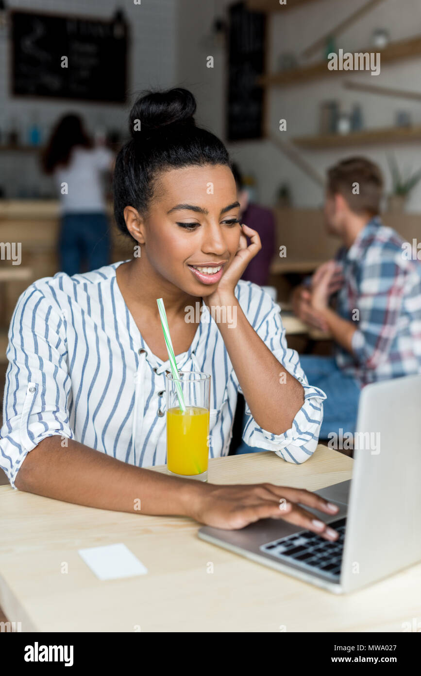beautiful smiling african american girl using laptop while drinking ...