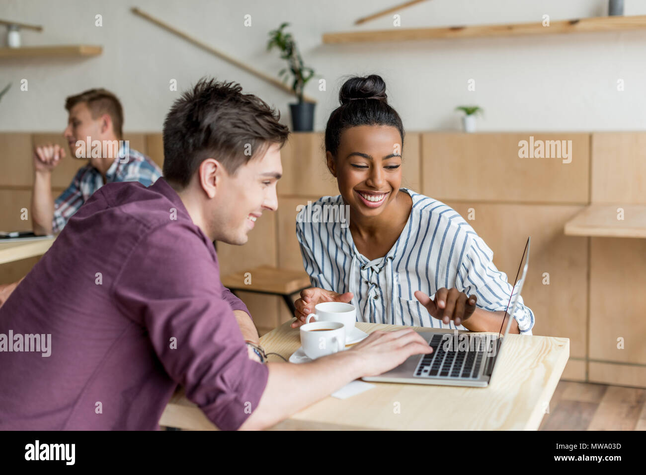 happy young multiethnic couple using laptop while drinking coffee in cafe Stock Photo