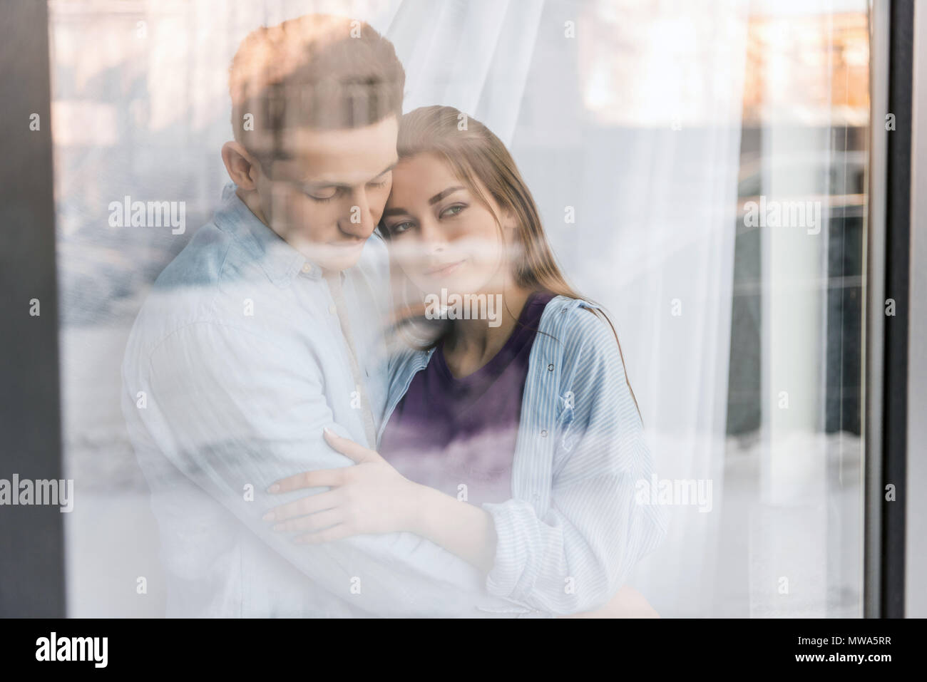 view through window on couple hugging and looking away Stock Photo - Alamy