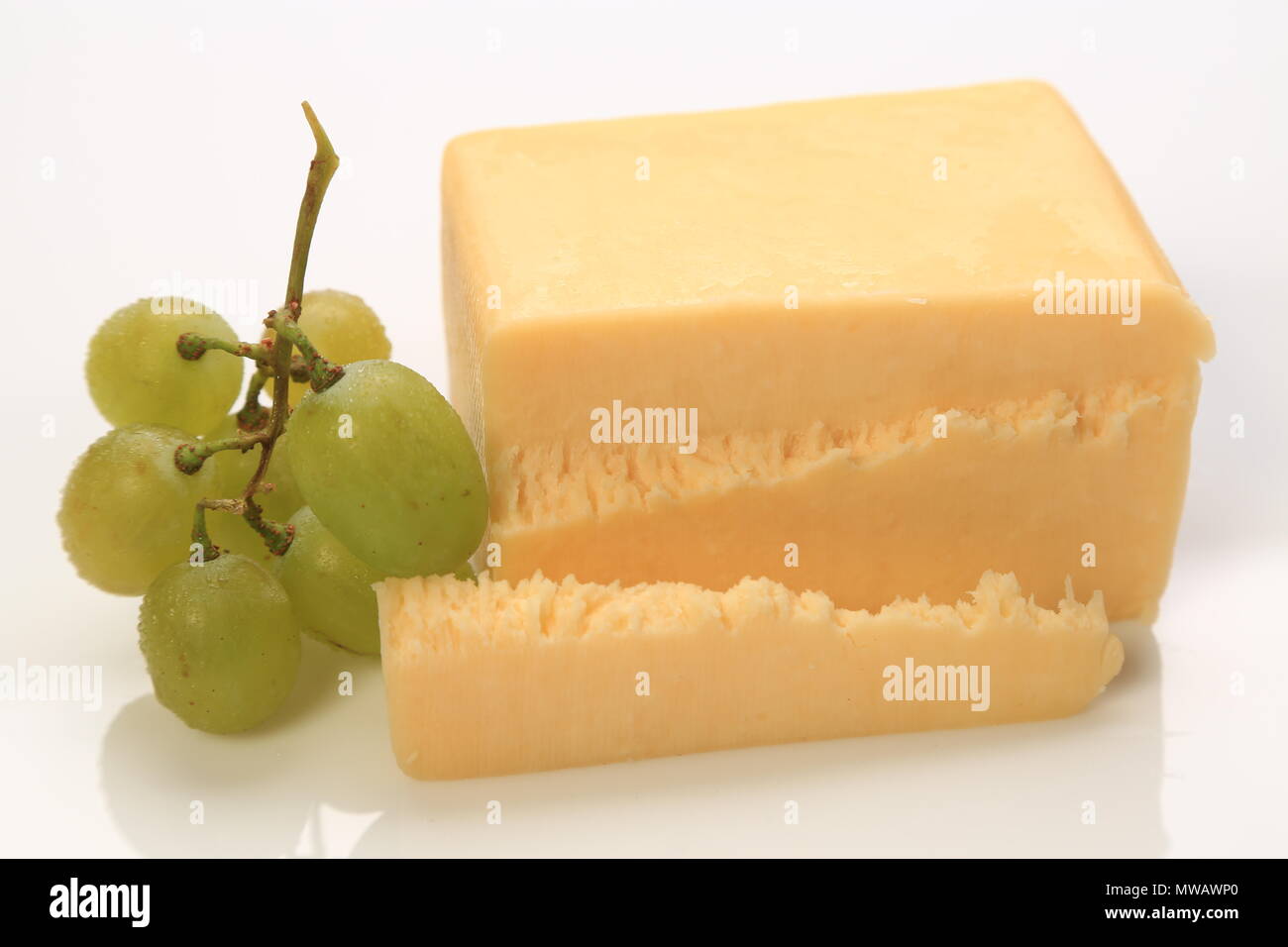 Sliced block of cheese with grapes on the side Stock Photo