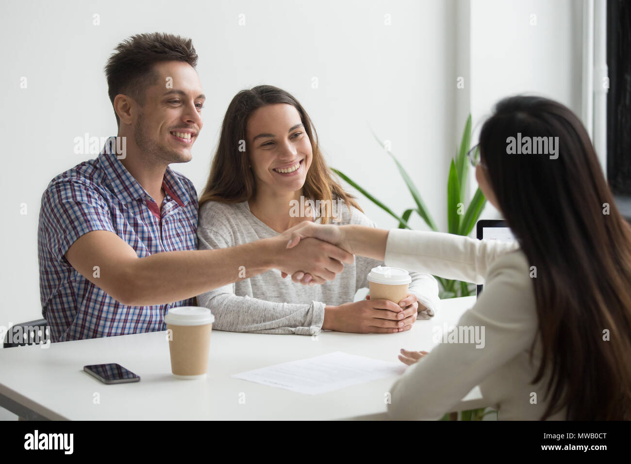 Smiling millennial couple handshaking realtor or advisor making  Stock Photo
