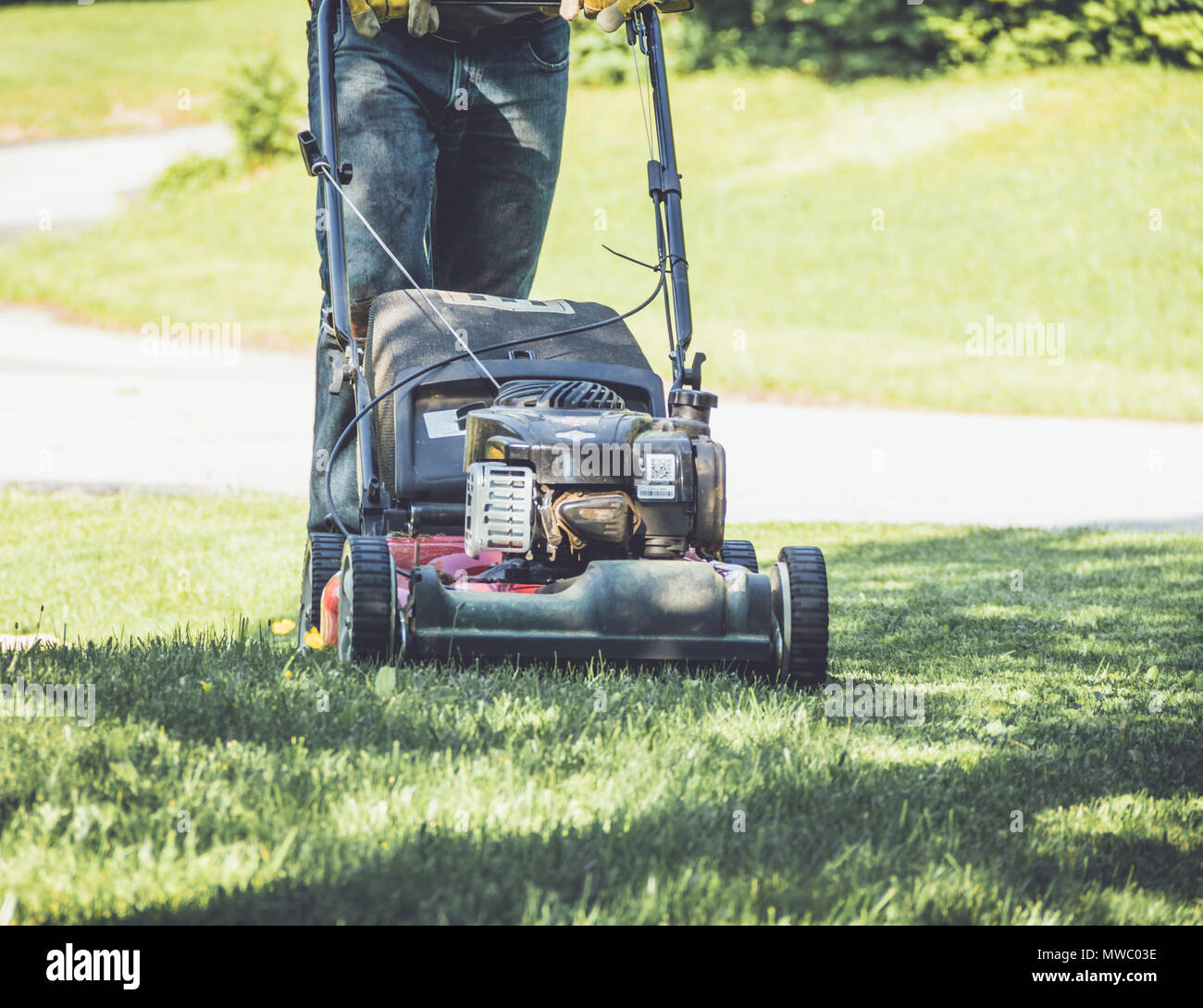 Red lawn mower cutting grass being pushed across a residential lawn by