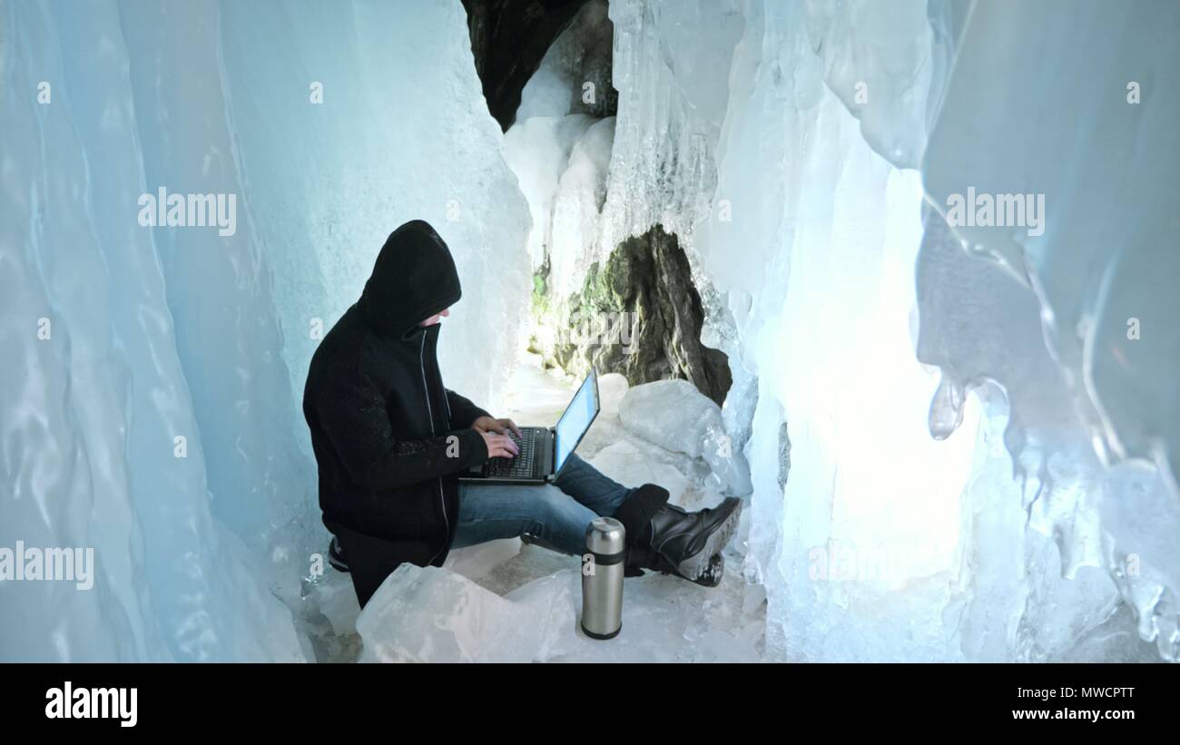 Hacker hacks the server. Man to program on laptop in ice cave. Around the  mysterious ice grotto. Man hides himself in a hood. Hacker has criminal  case Stock Photo - Alamy
