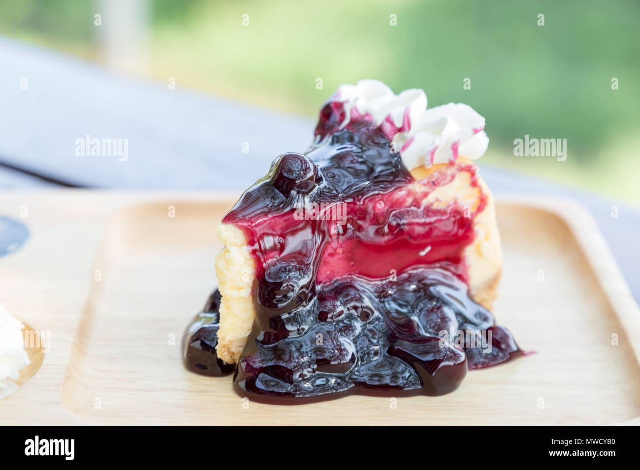 Blueberry cheesecake with cream on wooden plate on wood table at restaurant. Stock Photo