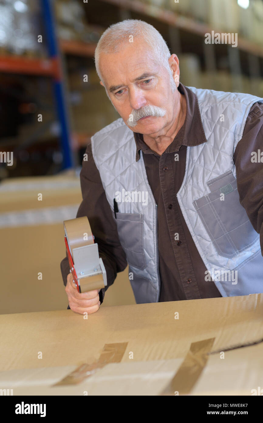 senior male worker sealing cardboard box with in warehouse Stock Photo
