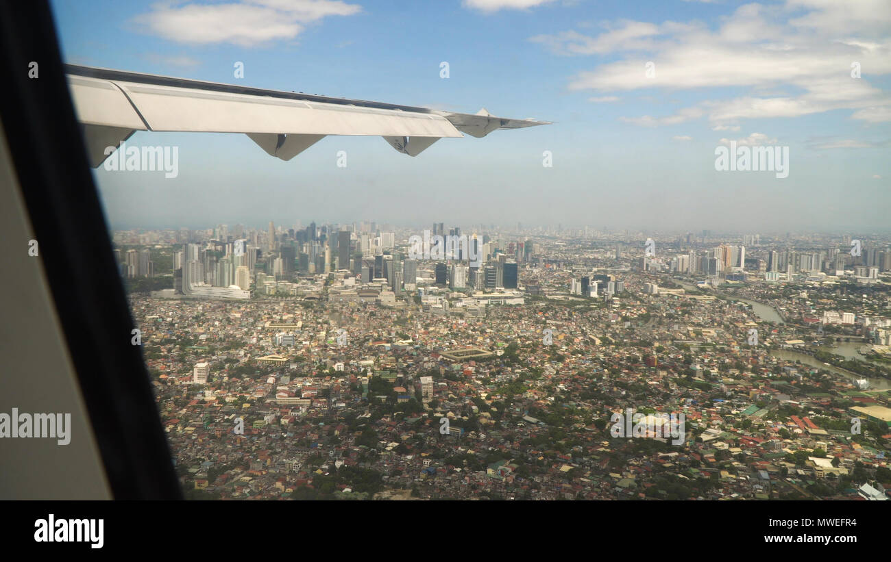 View through an airplane window on the city. Airplane window view showing wing of a plane flying over Manila. Aerial footage, Philippines. Travel concept. Stock Photo