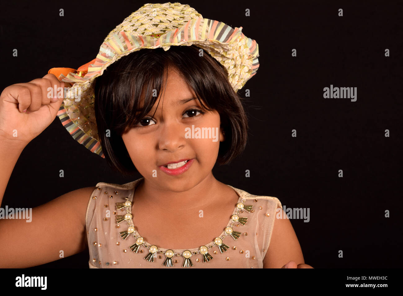 Little girl with a hat looking at camera against a black backdrop Stock