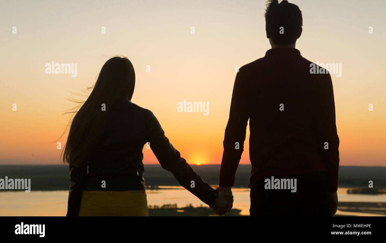Loving young couple holding hands looking each other at amazing sunset ...