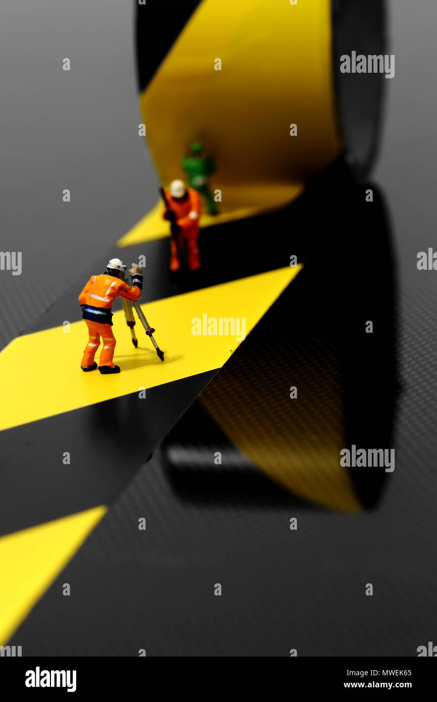 Miniature scale model construction workers using hazard tape on a carbon fibre surface Stock Photo