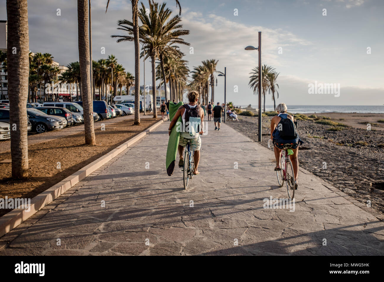 Surfer Cycling with Surfboard in hand. Stock Photo