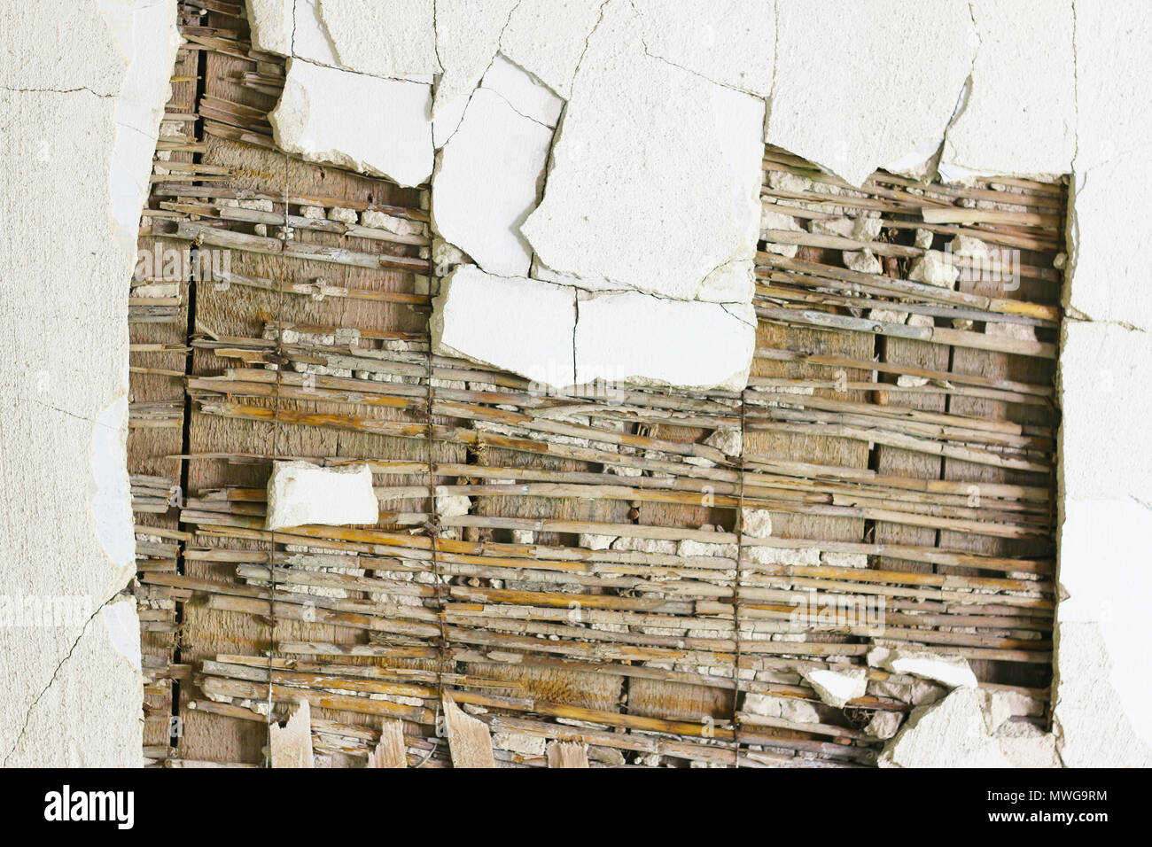 Ruined old white wall decoration. A hole in the wooden ceiling. Cracks in the plaster. Stock Photo