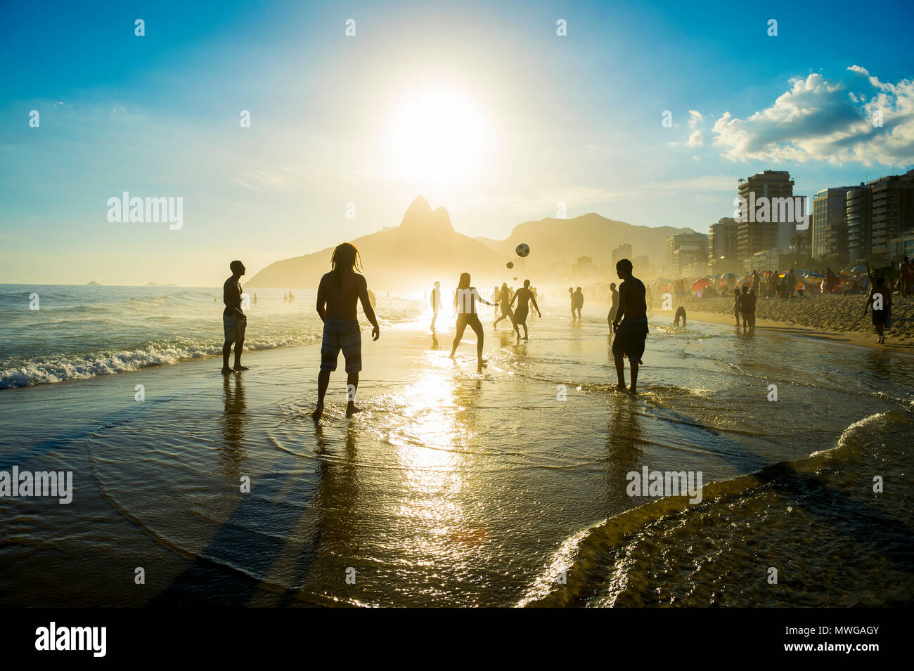 Distant sunset silhouettes playing keepy-uppie beach football on the sea shore in Ipanema Beach Rio de Janeiro Brazil Stock Photo