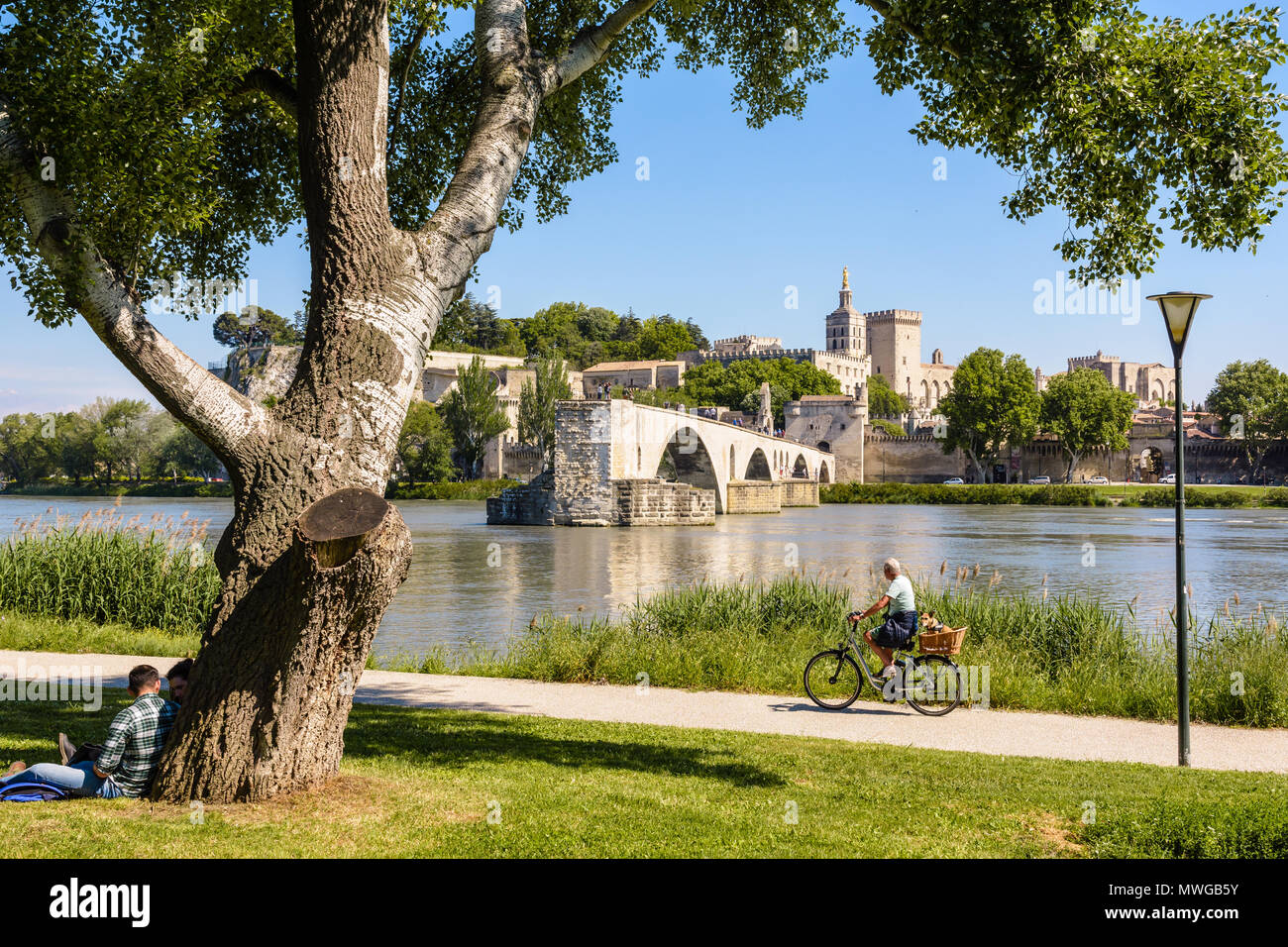 People biking or resting on the banks of the Rhone, opposite the Saint-Benezet bridge and the Papal palace by a sunny day in Avignon, France. Stock Photo