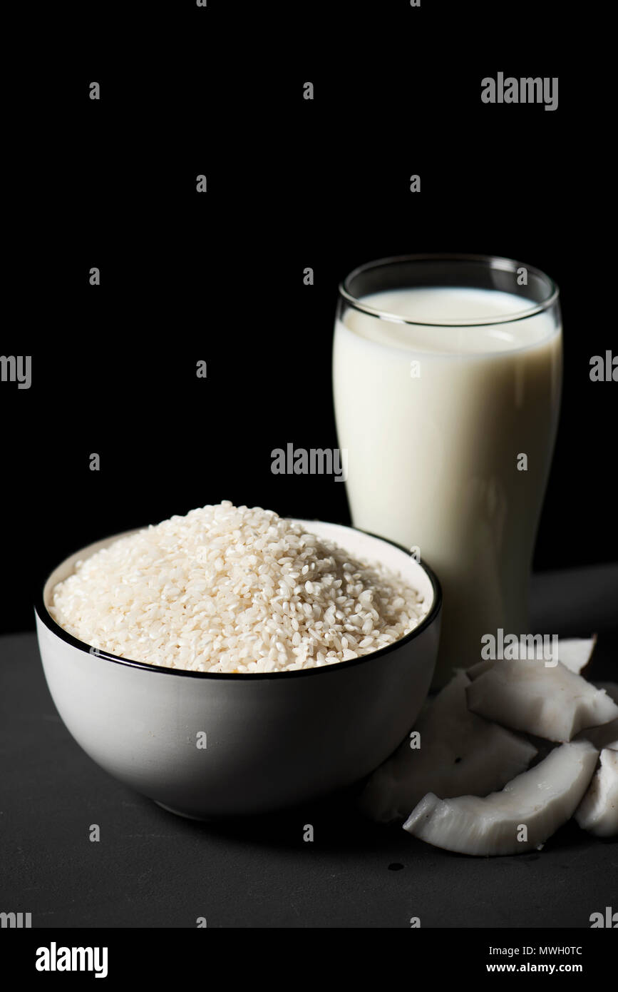 closeup of a bowl with rice, some pieces of coconut and a glass of rice and coconut milk on a gay rustic wooden table, against a black background with Stock Photo