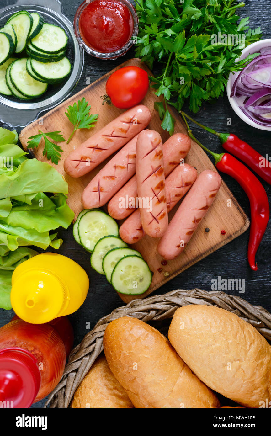 Juicy grilled sausages, sauces, fresh vegetables, crispy buns, on a wooden background. Top view. Flatlay. Ingredients for a hot dog. Street food. Stock Photo