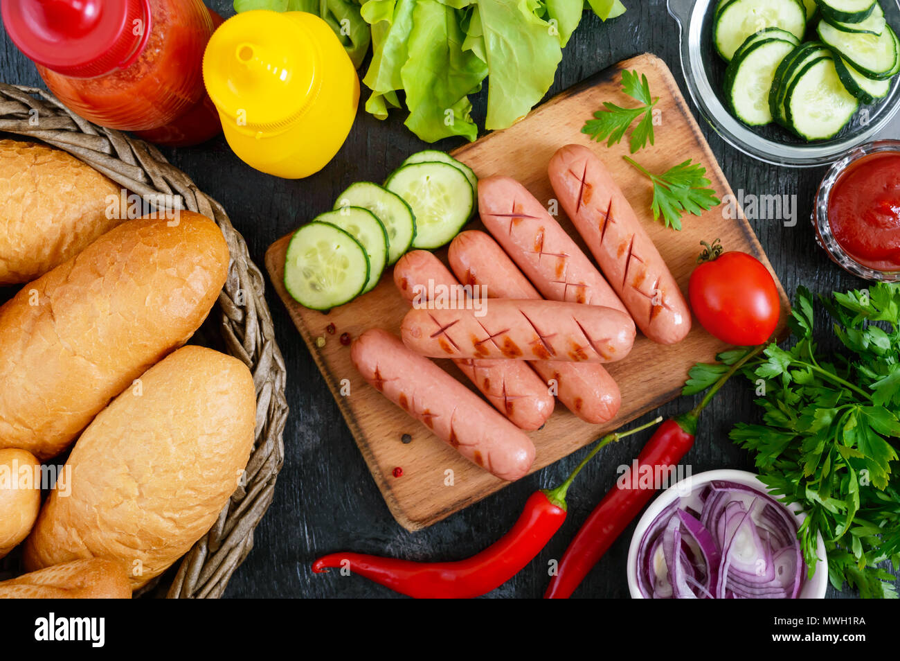 Juicy grilled sausages, sauces, fresh vegetables, crispy buns, on a wooden background. Top view. Flatlay. Ingredients for a hot dog. Street food. Stock Photo