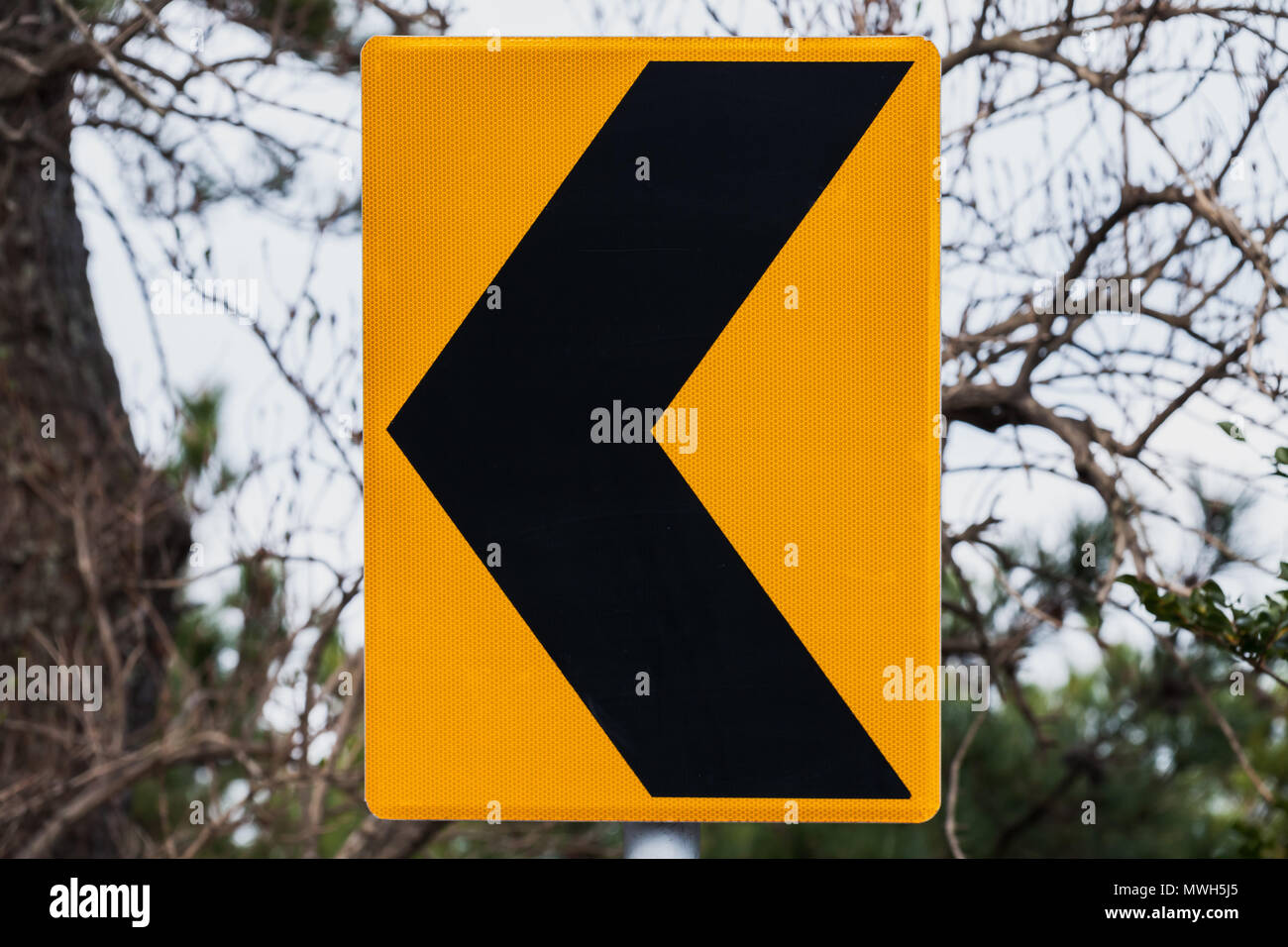 Dangerous turn left, yellow black road sign mounted on roadside Stock Photo