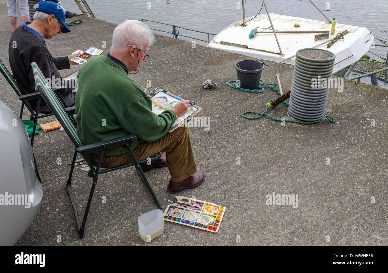 male elderly artists sat on a quayside painting the local  scenery with water colours. Stock Photo