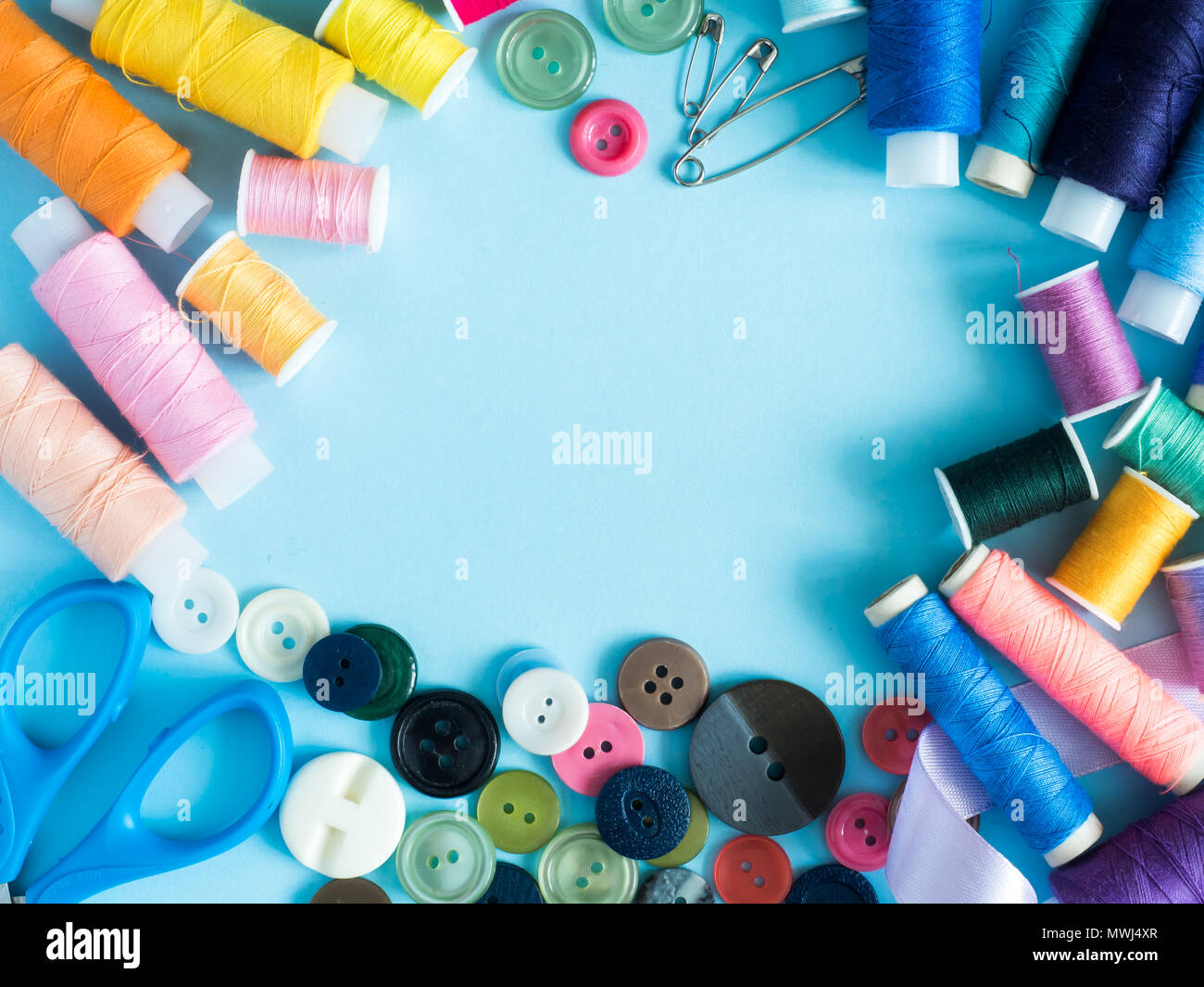Multicolored sewing threads and buttons on blue background with copy space flat lay. Stock Photo
