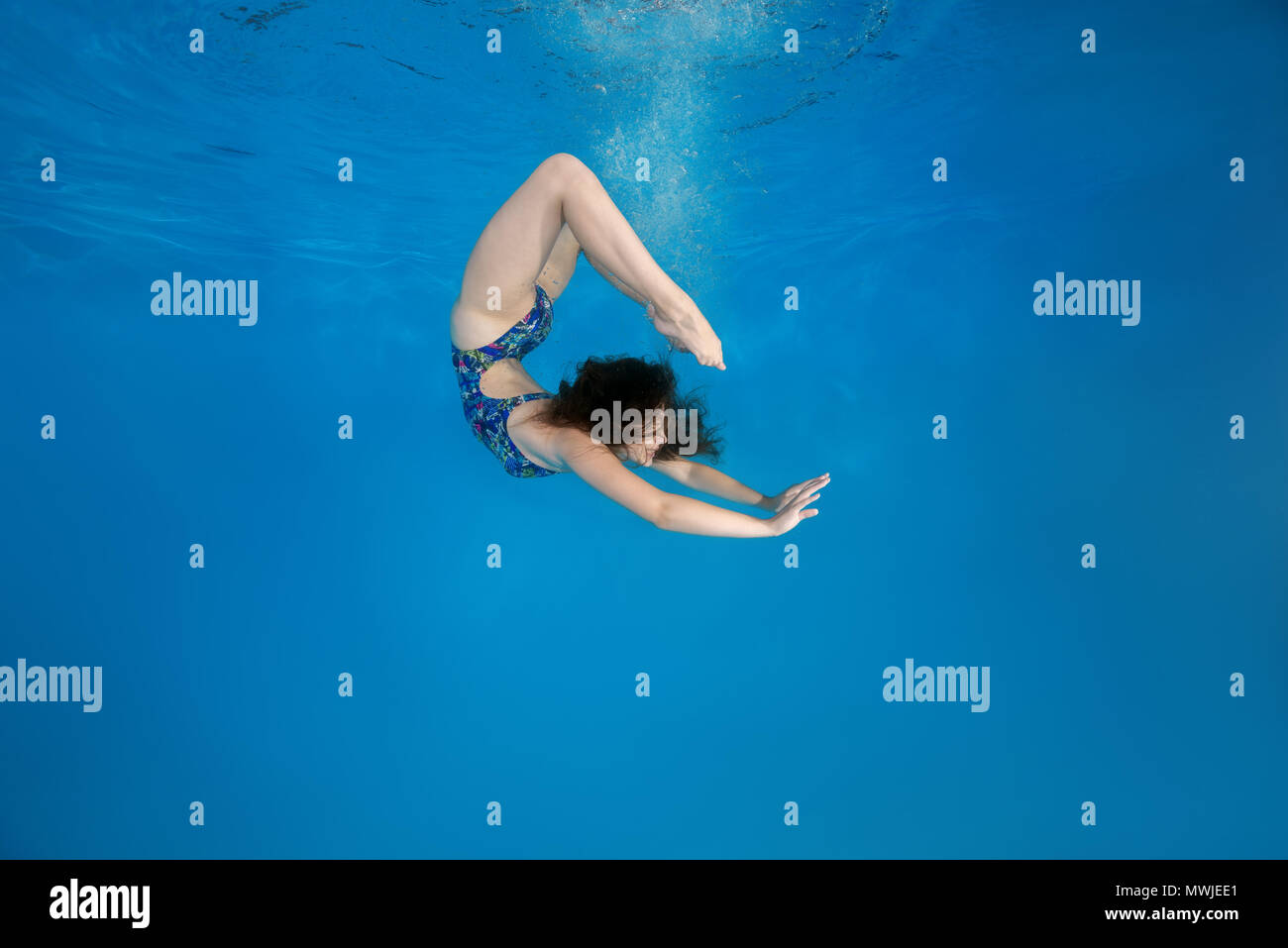 Girl curled into a wheel under water in the pool. Underwater acrobatics Stock Photo