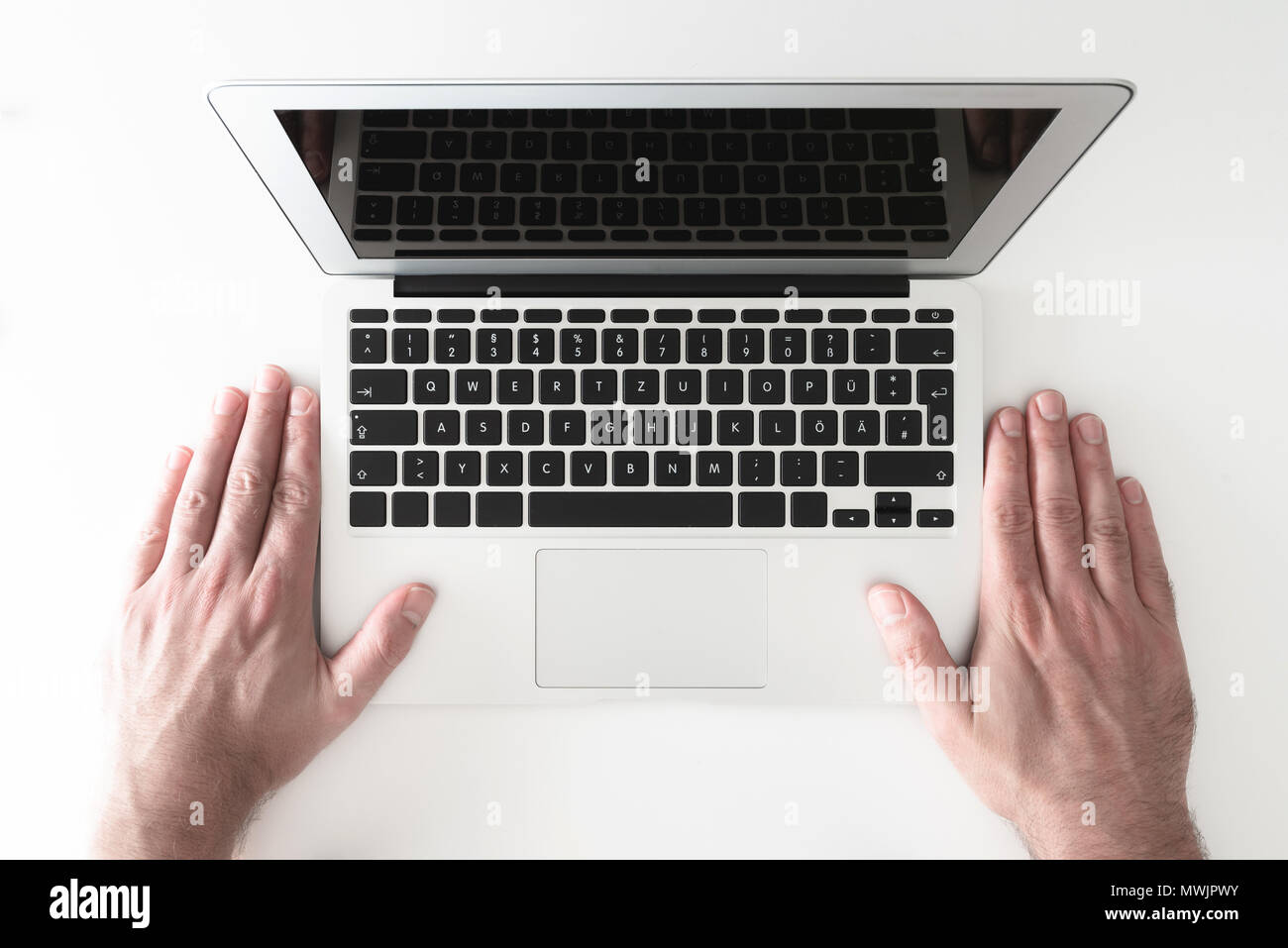 overhead shot of both hands of man placed besides notebook computer on white desk Stock Photo