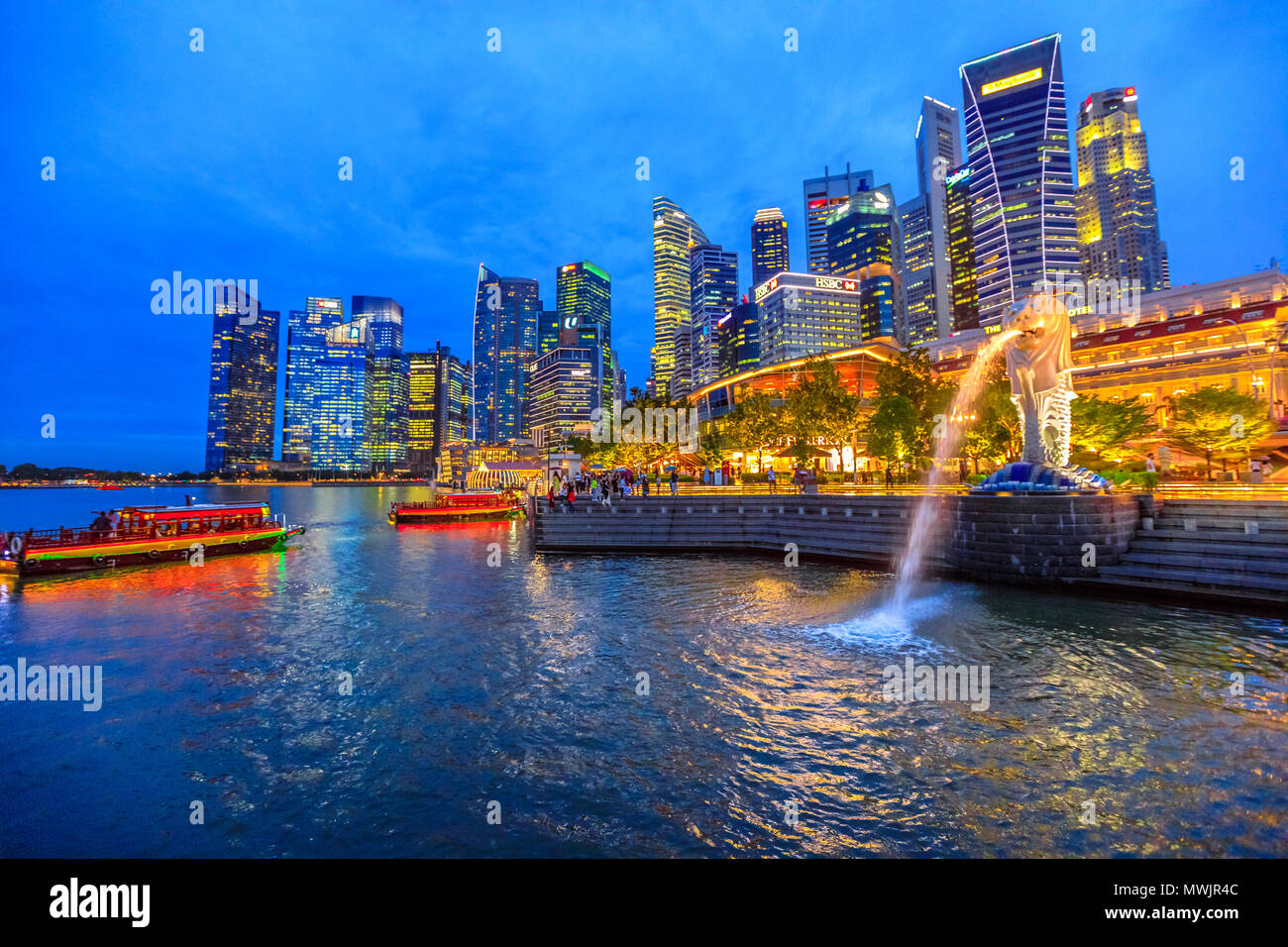 Singapore - April 27, 2018: Merlion Statue icon of Singapore with Central Business District or the CBD Buildings on background in Marina Bay, Central Area in Singapore at blue hour. Stock Photo