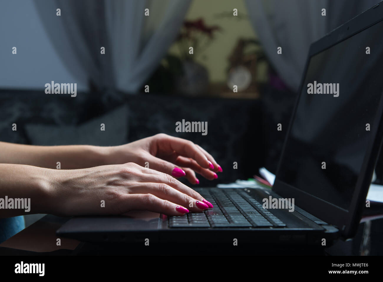 Female hands write something on the keyboard. The woman works hard at home at night or at night. Home office, work at home, earning on your own, self- Stock Photo