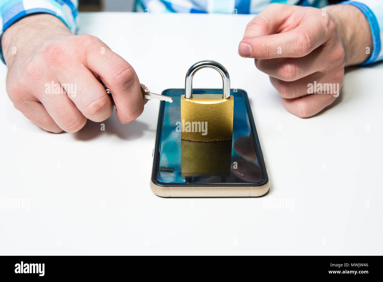 The man is holding a key to the padlock under the mobile phone. The concept of securing the phone, cyber attack, data security problems on a personal  Stock Photo
