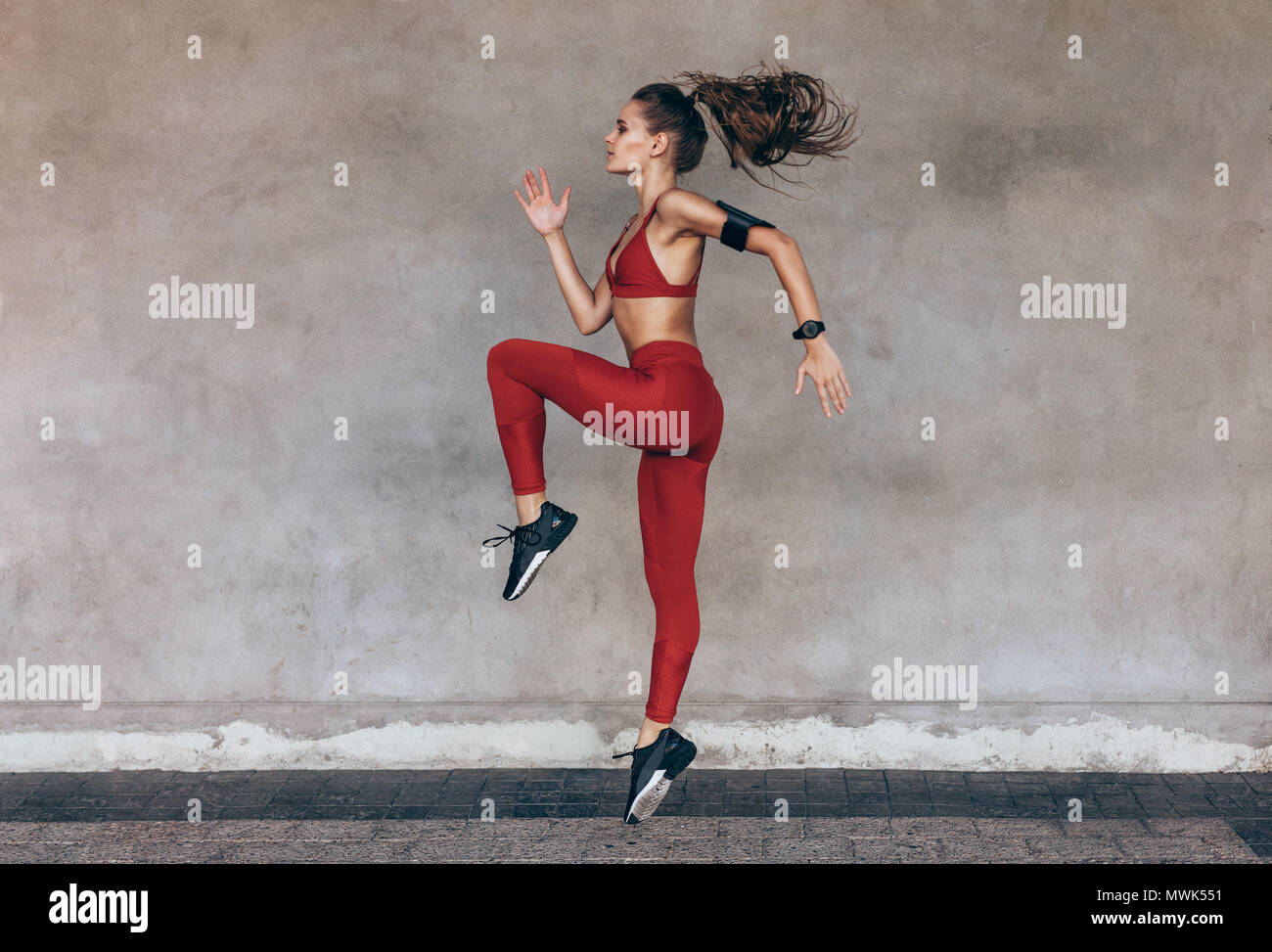 Sportswoman jumping and stretching. Full length of healthy female exercising and jumping outdoors. Stock Photo