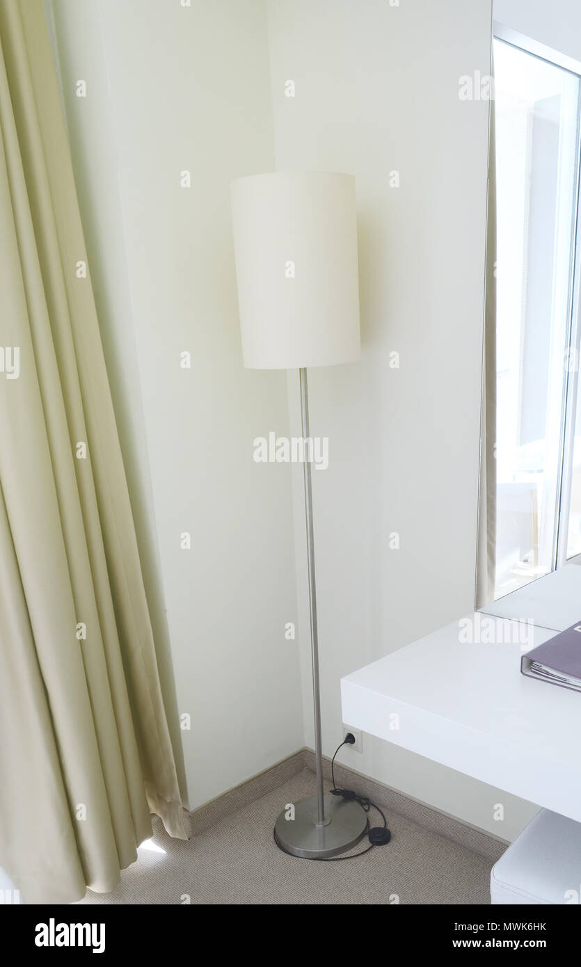 A floor lamp in the corner of the hotel room. A mirror and a console with a notebook Stock Photo