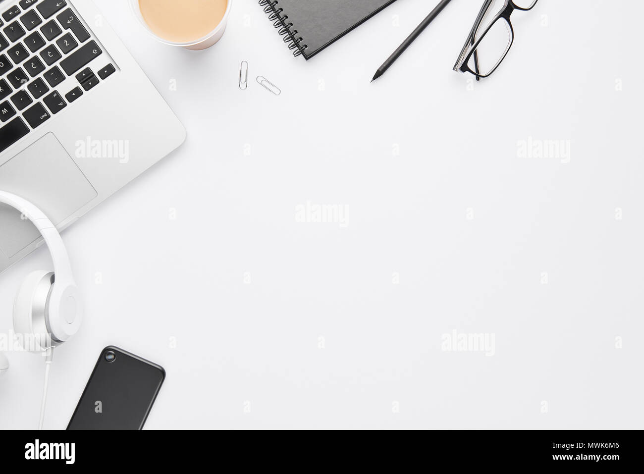 Work space concept. Top view of laptop, white headphones, black cell phone, notebook, glasses and coffee on white background with copy space. Flat lay Stock Photo