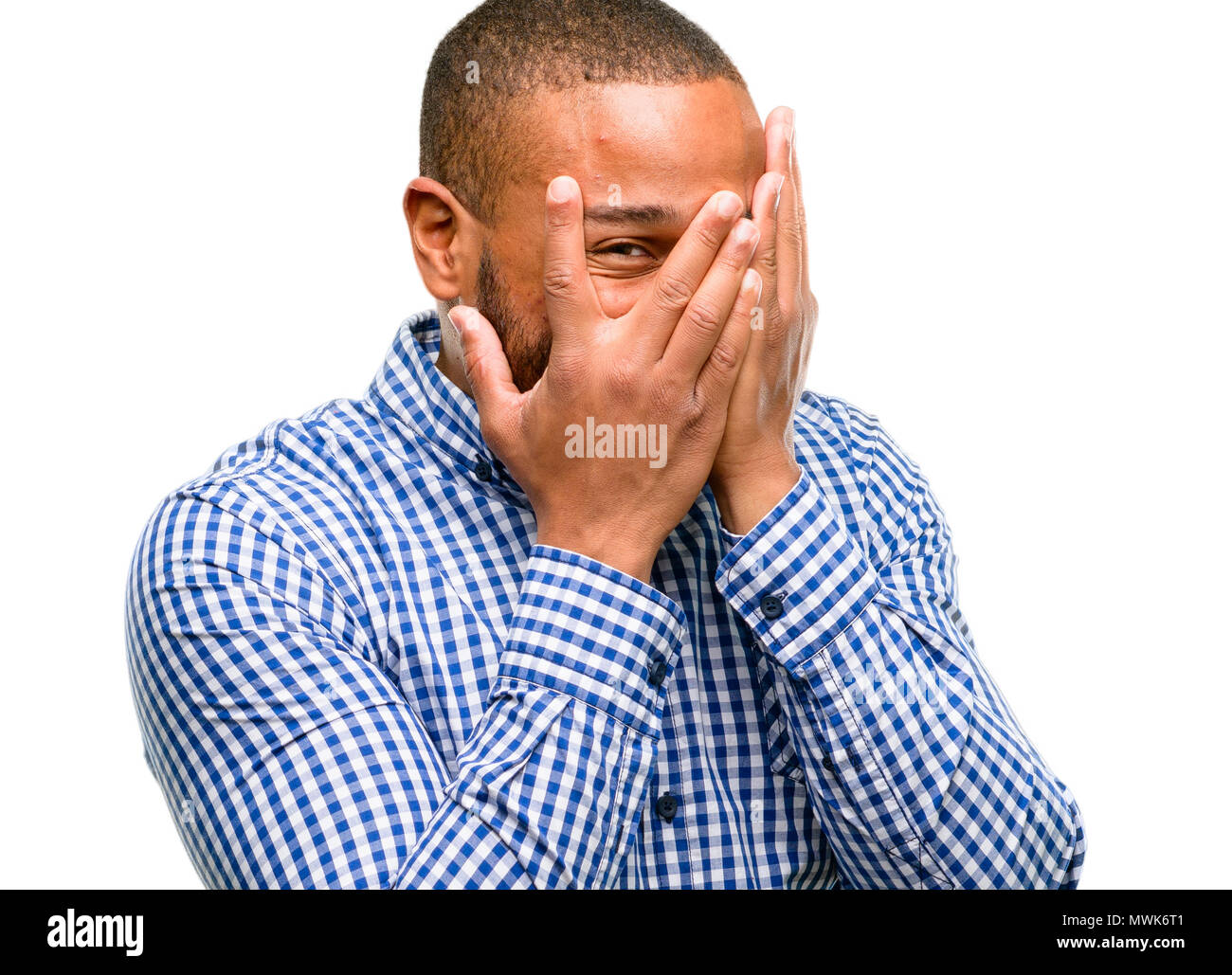 African american man with beard smiling having shy look peeking through fingers, covering face with hands looking confusedly broadly isolated over whi Stock Photo