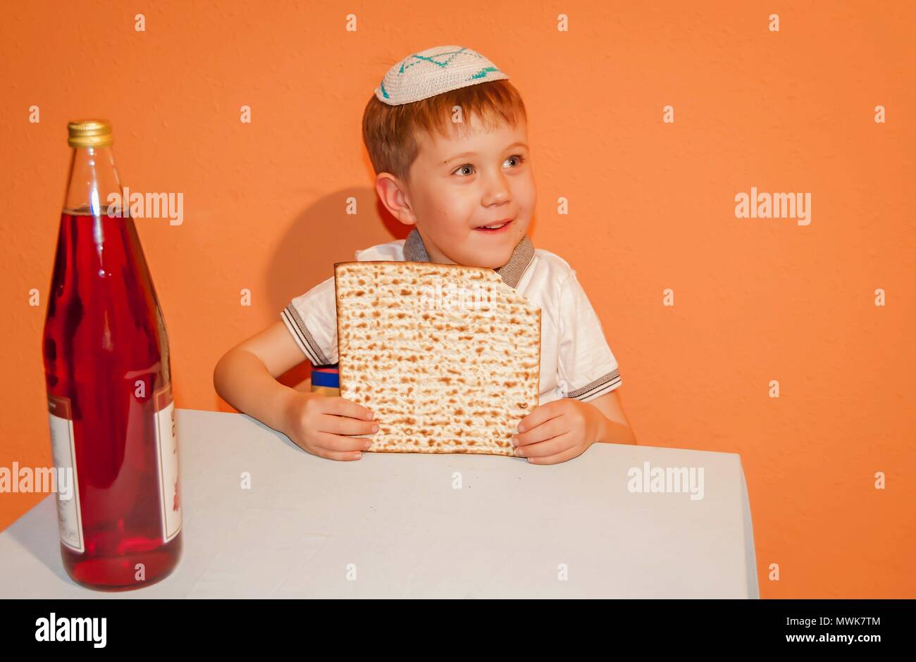 Little Caucasian child with a kippah on his head eating matzah. Jewish Passover illustration. Stock Photo