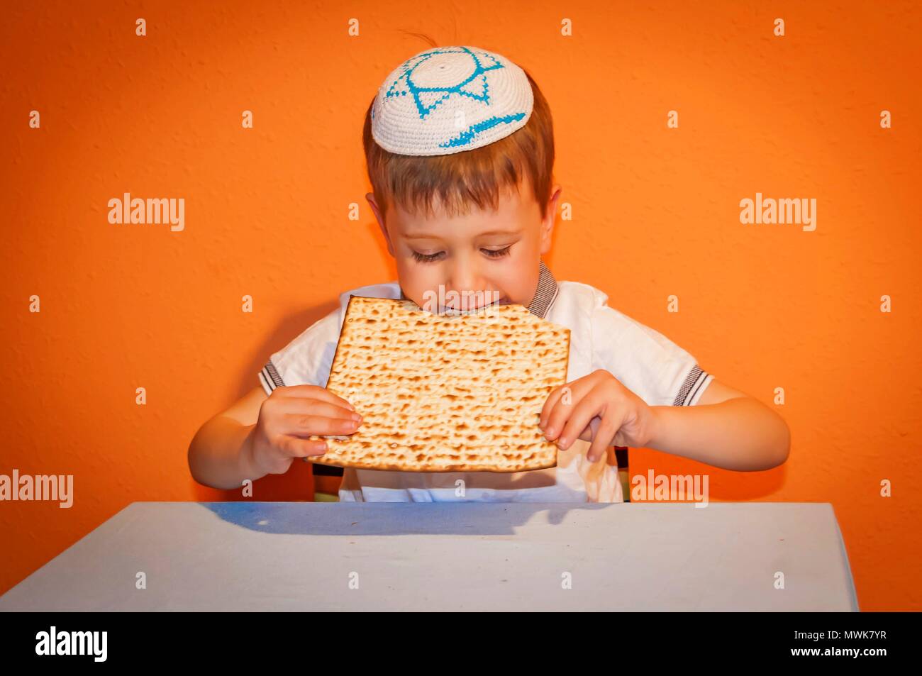 Happy little Jewish child with a kippah on his head eating matzo bread during the Jewish holiday of Pessach. Passover illustration. Stock Photo