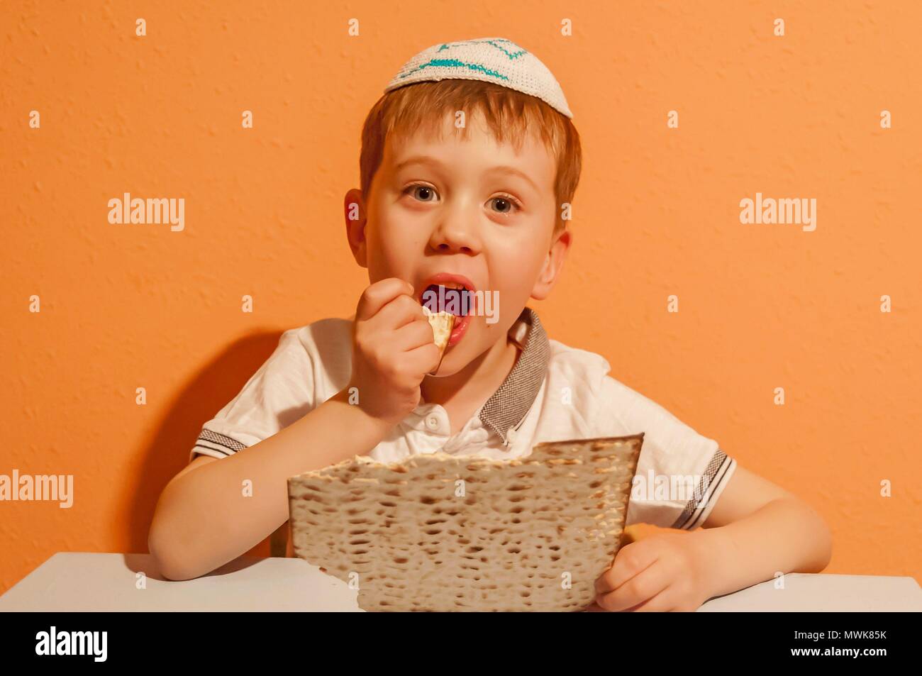 Happy little Jewish child with a kippah on his head eating matzo bread during the Jewish holiday of Pessach. Passover illustration. Stock Photo