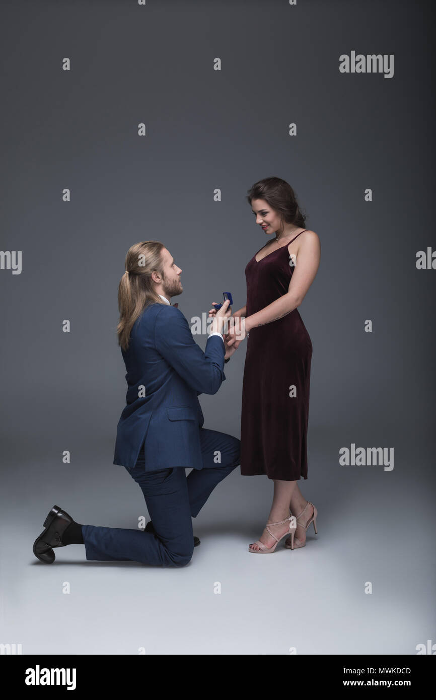 young man in tuxedo making marriage proposal to his girlfriend while standing on one knee Stock Photo