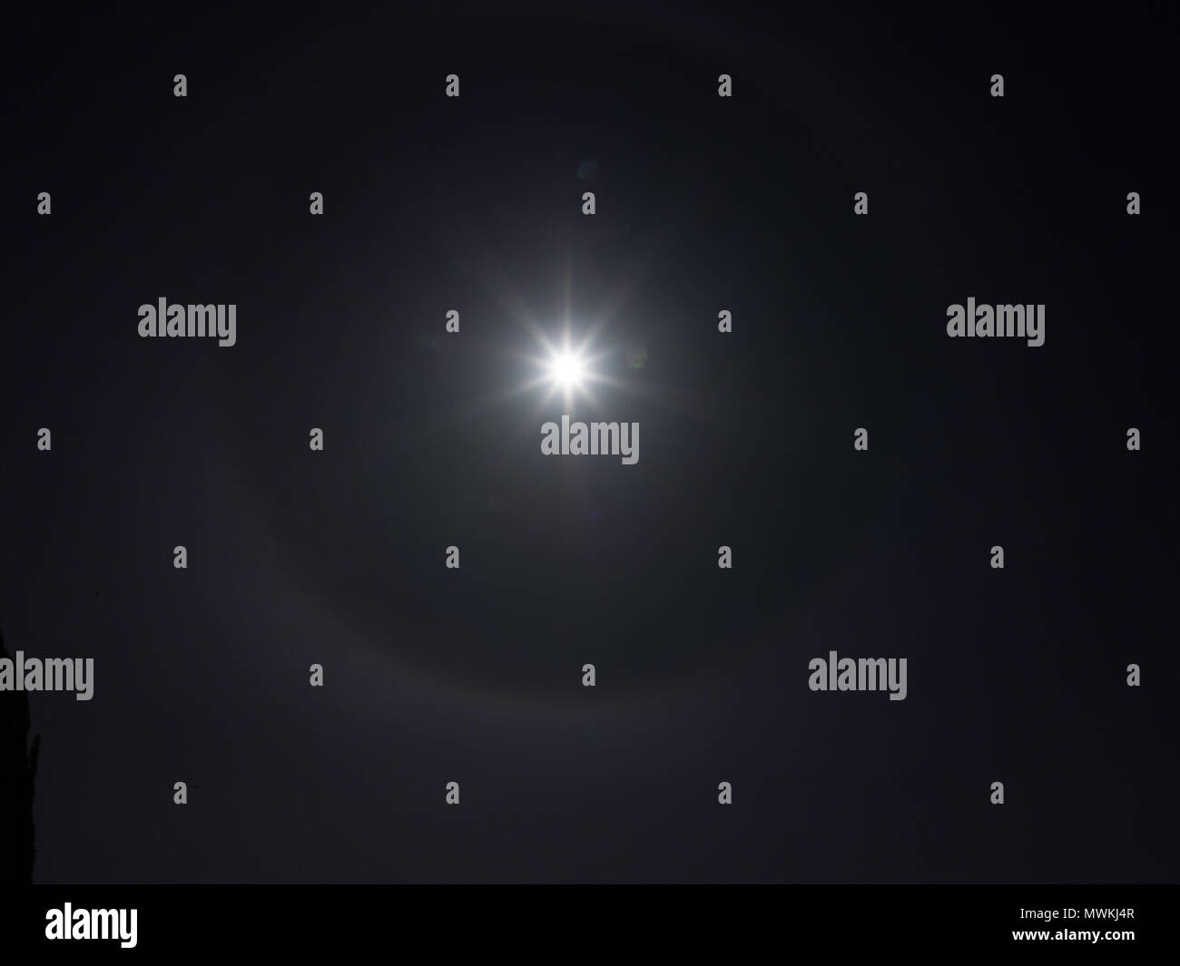 Sun dog surrounding the sun in a dark sky slightly visible Stock Photo