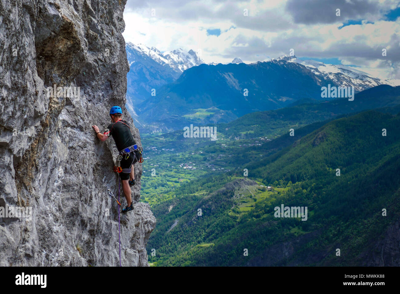 Rock climber in blue helmet high above the Durance Valley, near Briancon, Ecrins, French Alps Stock Photo