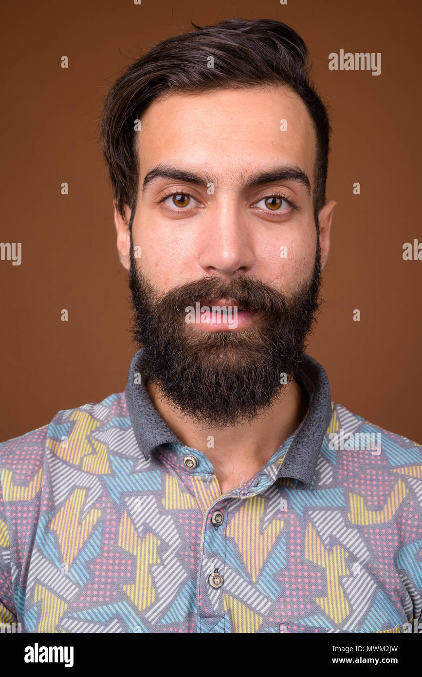 Young handsome bearded Persian man against brown background Stock Photo